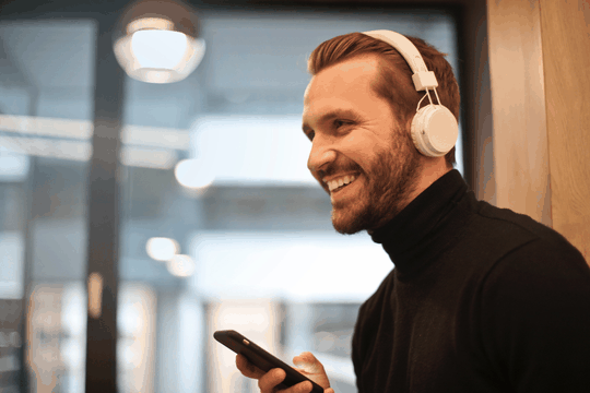 Uśmiechnięty mężczyzna w słuchawkach patrzący na telefon